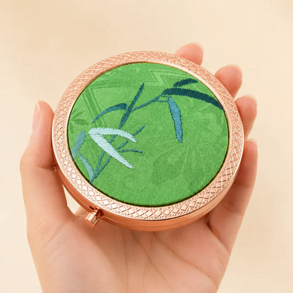 Green Bamboo hand-embroidered silk compact mirror held in the hand